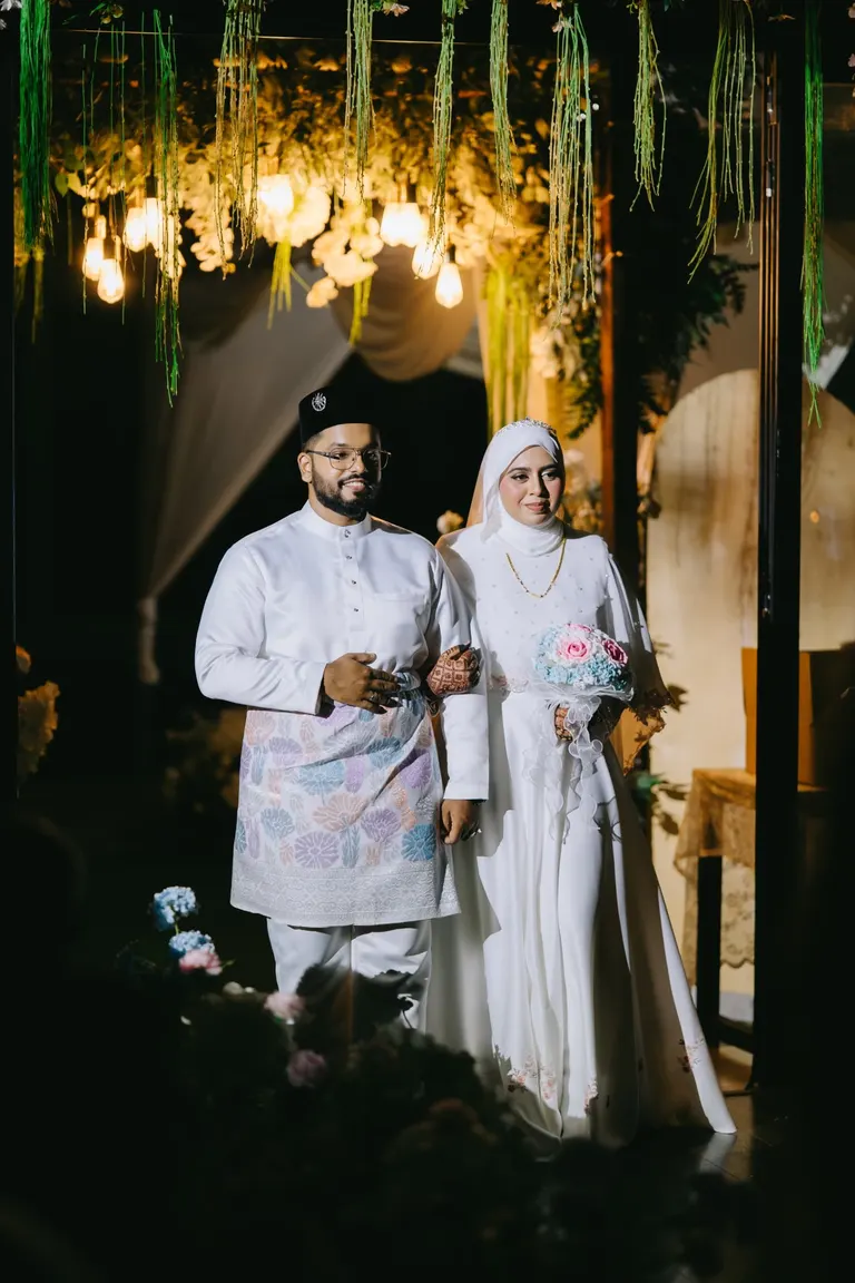 A couple walking in at night in matching white outfits under hanging lights